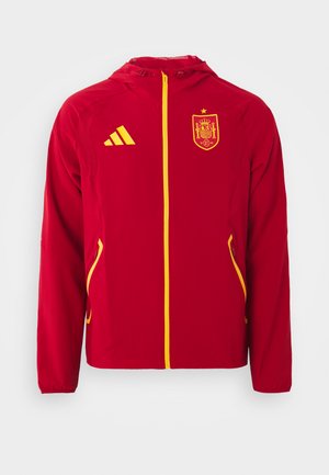 Rote Jacke mit Kapuze, gelben Akzenten und Reißverschluss. Verfügt über ein Spanien-Wappen auf der Brust und zwei seitliche Taschen. Glattes, leichtes Material.