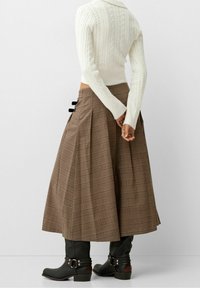 Brązowa kraciasta spódnica z zakładkami, z wysokim stanem, ozdobiona czarnymi wstążkami. Do tego czarne kozaki do kolan oraz kremowy teksturowany sweter w warkocze.