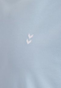 Ljusblått tyg med en slät yta. Ett vitt grafiskt element som liknar två chevrons är placerat på vänster sida.