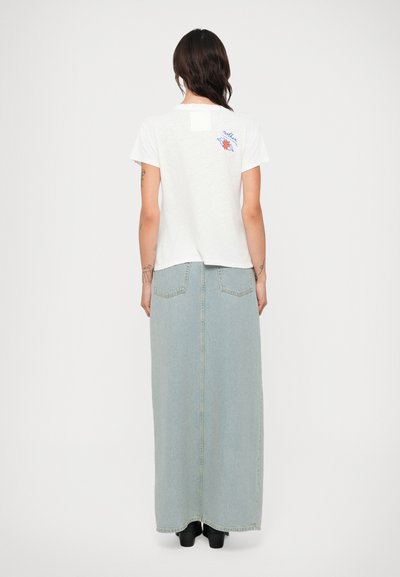 Tricou alb cu mânecă scurtă și imprimeu pe spate, purtat cu o fustă lungă din denim de culoare albastră deschisă, cu două buzunare pe spate și croială dreaptă.