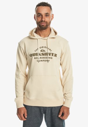 Beige hoodie featuring a front kangaroo pocket, drawstring hood, and dark brown "Quiksilver" logo with curved text design. Soft fabric texture.
