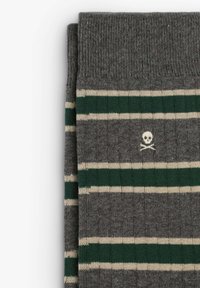 Graue Socken mit horizontalen Streifen in grün und creme, die an der Seite ein kleines weißes Totenschädel- und Kreuzbones-Logo aufweisen. Stricktextur.