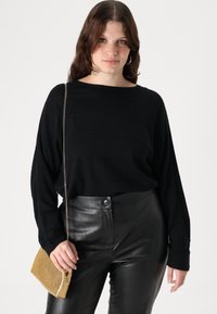 Črna dolga majica s širokim ovratnikom, v kombinaciji z visokim črnim usnjenim hlačami. Drži zlat kovinski clutch.