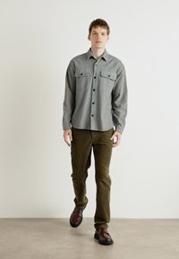 Chemise grise à boutonner avec deux poches avant, associée à un pantalon vert olive et des chaussures marron ; texture lisse et coupe standard.