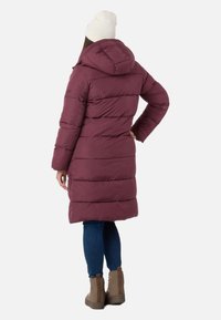 Mørkerød puffjakke med hætte, med vandret quiltede sektioner. Kombineret med mørke jeans og lysebrune ankelstøvler.