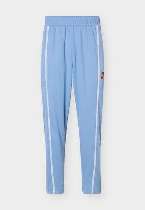 Pantalon de sport bleu clair avec bandes blanches sur les côtés et taille élastique, doté d'un petit patch logo multicolore sur la cuisse droite.