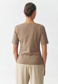 Haut marron à manches courtes avec un col rond, fabriqué à partir d'un matériau lisse et ajusté. Présente un design simple et un ourlet légèrement arrondi.