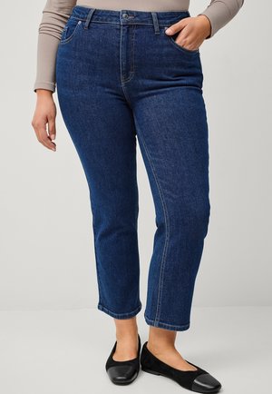Dark blue denim jeans with a straight cut, featuring front pockets, a zip fly, and stitched detailing. Paired with black flats.