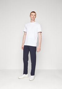 Weißes Kurzarm-T-Shirt mit marineblauen Akzenten, kombiniert mit marineblauen Hosen und weißen Sneakers, das eine klare, moderne Schnittführung und ein minimalistisches Design aufweist.