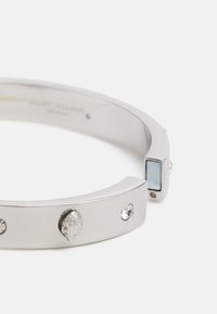 Bracciale d'argento con un filo liscio e piatto, caratterizzato da un accento geometrico con una lastra blu chiaro e tre pietre trasparenti incastonate.
