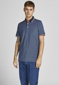 Marineblå polo-shirt lavet af bomuld, med en klassisk krave med rød og hvid stribe, tre knapper og et lille logo på brystet.