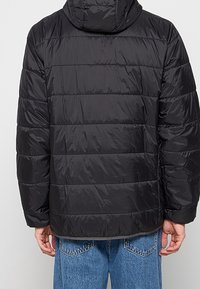 Czarna ocieplana kurtka z kapturem, z poziomym pikowaniem i gładką nylonową teksturą. Widoczne szwy i elastyczne mankiety.