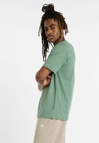 Kortærmet grøn t-shirt lavet af blødt stof med en afslappet pasform. Har en rund hals og subtile syninger. Sammen med beige bukser.