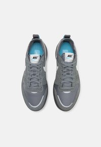 Sivi atletski tenisici z mrežastim in semiš zgornjim delom, izrazitim belim Nike znakom in modrim notranjim oblogo. Ravne vezalke in oblazinjen jezik.