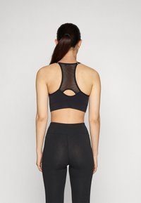 Sostenedor deportivo negro con inserción de malla, diseño de espalda racer, y un detalle de corte en la parte posterior, combinado con unas mallas negras de cintura alta.