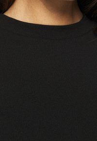 Czarna żebrowana tkanina z dopasowanym, okrągłym dekoltem. Tekstura jest gładka z pionowymi liniami na całej powierzchni, co wskazuje na elastyczność.