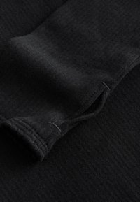 Tessuto nero con motivo lavorato a maglia testurizzato. È visibile il bordo di un risvolto, con una finitura pulita e una cucitura sottile.