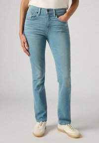 Vaqueros de mezclilla azul claro con corte recto, diseño de cinco bolsillos y un ligero desgastado. Combinados con zapatillas blancas para un look casual.