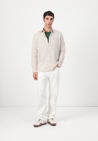 Plaid button-up shirt in beige and brown over a green shirt, paired with white trousers and two-tone sneakers. Simple design, no patterns.