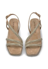 Des sandales en daim beige présentent quatre brides entrecroisées ornées de reflets dorés scintillants, un design ouvert à l'avant et un talon carré.