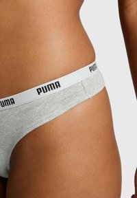 Graue Baumwollslip mit breitem weißen Bund, der mit schwarzem "PUMA"-Branding versehen ist. Weicher Stoff, tief sitzendes Design und minimale Bedeckung.