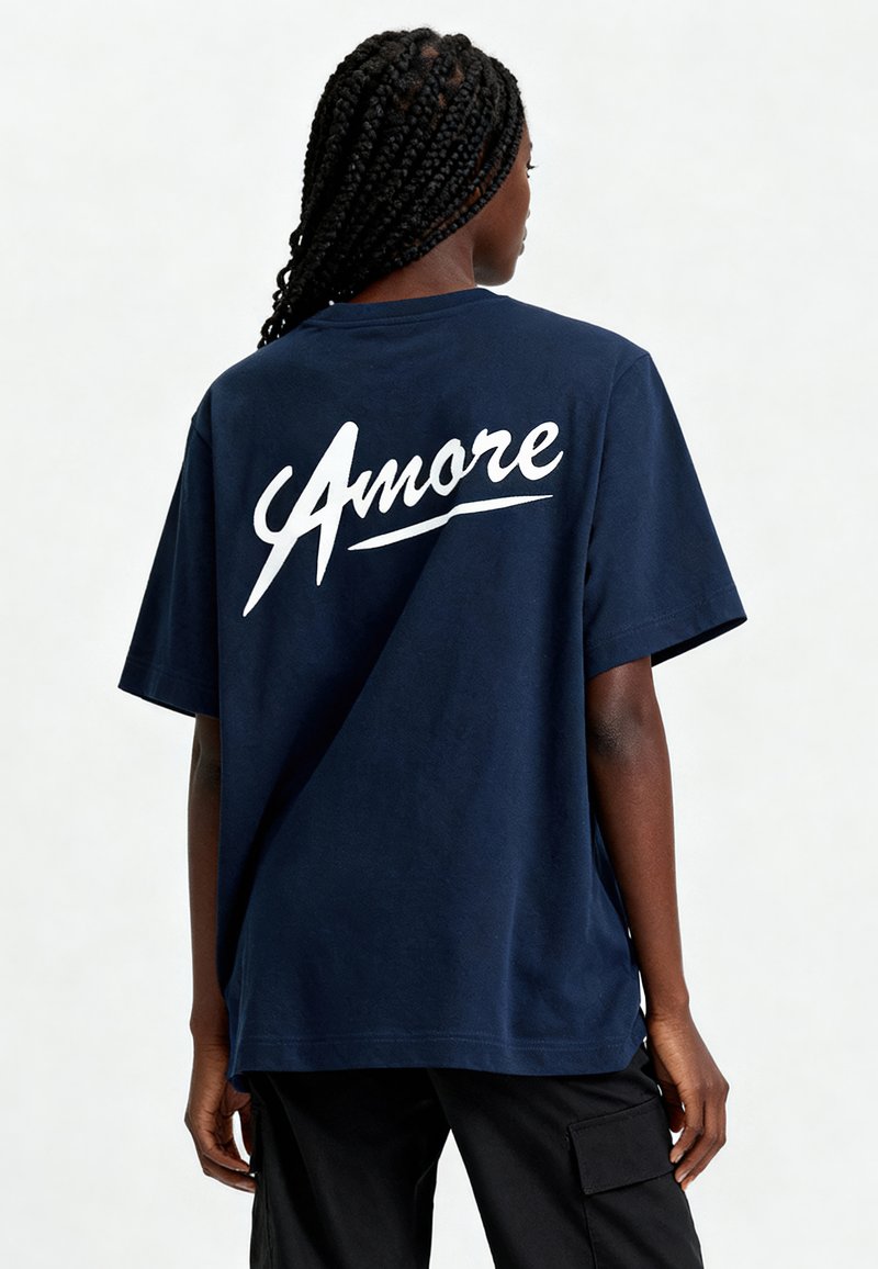Kļavu zila kokvilnas t-krekls ar īsām piedurknēm un brīvu piegriezumu. Vārds "Amore" ir izdrukāts baltā, kursīvā uz aizmugures. Gluda tekstūra.