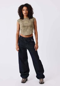 Top de ante verde olivo recortado con mangas cortas, combinada con jeans baggy azul oscuro. Calzado con un material texturizado en gris.
