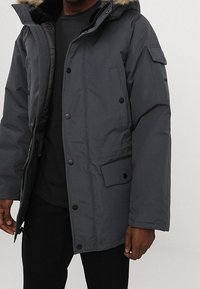 Ciemnoszara ocieplana parka z zapięciem na zamek i guziki, kaptur wyłożony futrem, kieszenie po bokach oraz strukturalny materiał. Charakteryzuje się luźnym krojem.