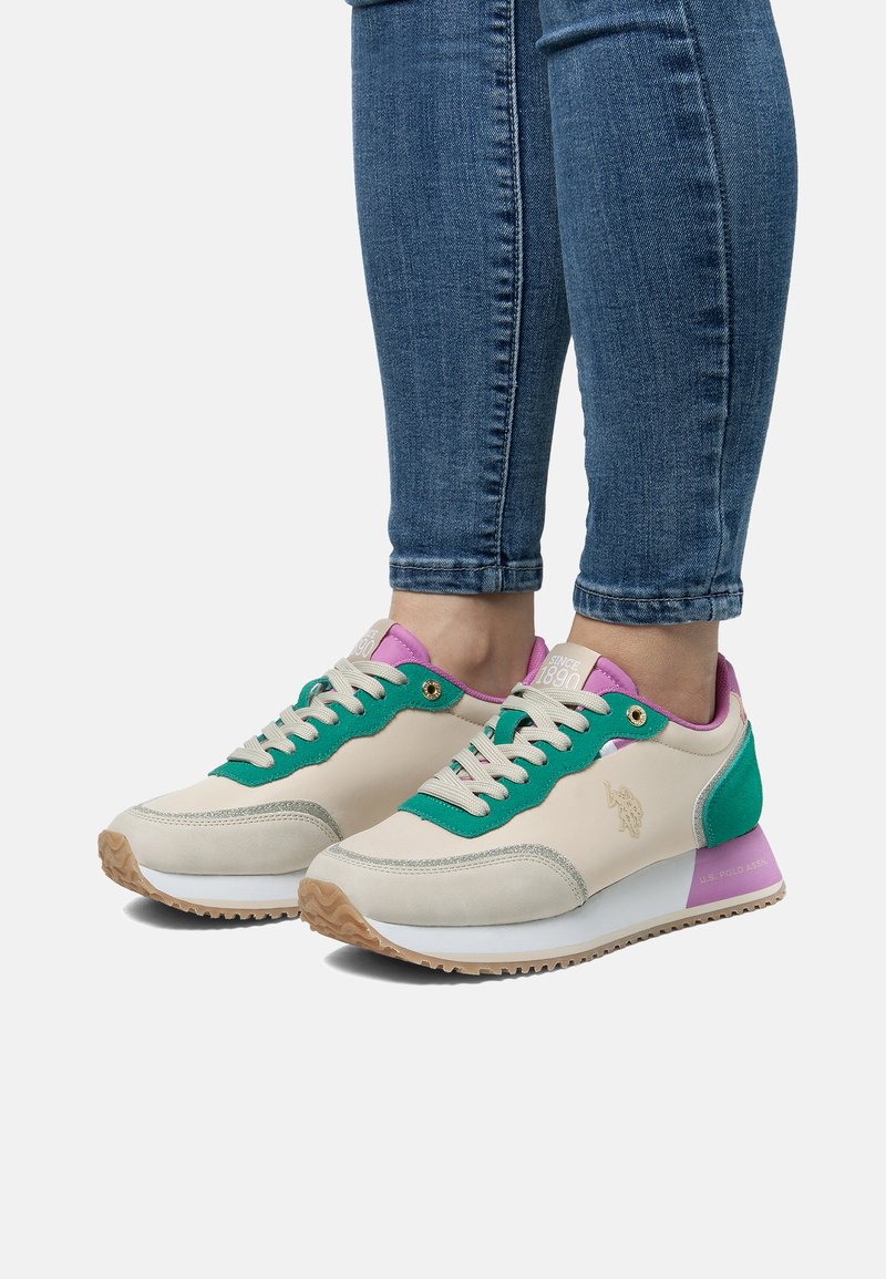 Sneakers har en krämfärgad ovandel med gröna och lila accenter, texturerade material, runda snören och en dämpad sula med en kontrasterande yttersula.