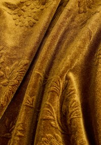 Luxuriöser senfgelber Samt mit weicher Textur, der ein florales Muster zeigt, das tief eingeprägt ist und eine reichhaltige Farbgebung aufweist.