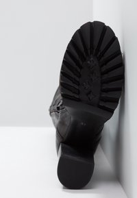 Stivale in pelle nera con superficie texturizzata, tacco robusto e suola in gomma scanalata con un motivo di stelle e esagoni. Taglia contrassegnata come 37.