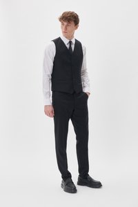 Schwarzer Dreiteiler mit maßgeschneiderter Weste, weißem Hemd und schwarzen Hosen, ergänzt durch schwarze Anzugschuhe.