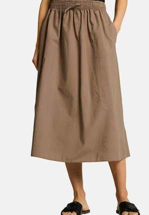 Frau trägt einen braunen Midirock mit elastischem Bund und Kordelzug, kombiniert mit schwarzen Schlupfsandalen.