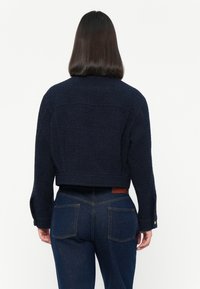 Navy blue cropped jacket made of textured fabric with a wide collar and buttoned cuffs. Features a leather patch labeled "MALINA" at the back.