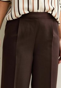 Bruine broek met een gladde textuur, met een hoge taille en zichtbare plooien aan de voorkant, gecombineerd met een gestreepte blouse.