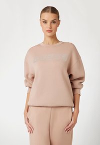 Felpa rosa chiaro con una vestibilità rilassata e polsini a costine. Caratterizzata da "GUESS" in strass argentati sulla parte anteriore. Tessuto misto cotone.