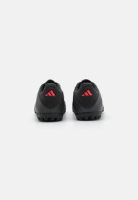 Black sports shoes with red accents, textured synthetic material, low profile design, and rubber studs on the outsole for traction.