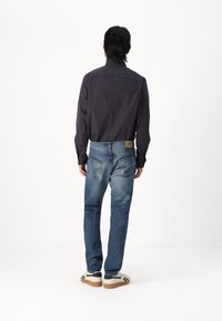 Camisa de manga larga a rayas navy combinada con jeans de lavado medio, con un ajuste clásico, bolsillos traseros y zapatillas blancas con detalles en negro.