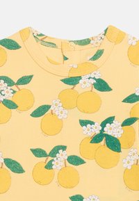 Κίτρινο ριγωτό ύφασμα με πρ άσινα φύλλα, λευκά άνθη και κίτρινο μοτίβο φρούτων, με στρογγυλή λαιμόκοψη και ένα κούμπωμα με κουμπί