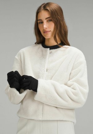 Valkoinen pörröinen takki, jossa on pyöreä kaula-aukko ja hakasulku. Ominaisuuksiin kuuluvat leveät mustat hihansuut ja mustat käsineet. Pehmeä rakenne, lyhennetty malli.