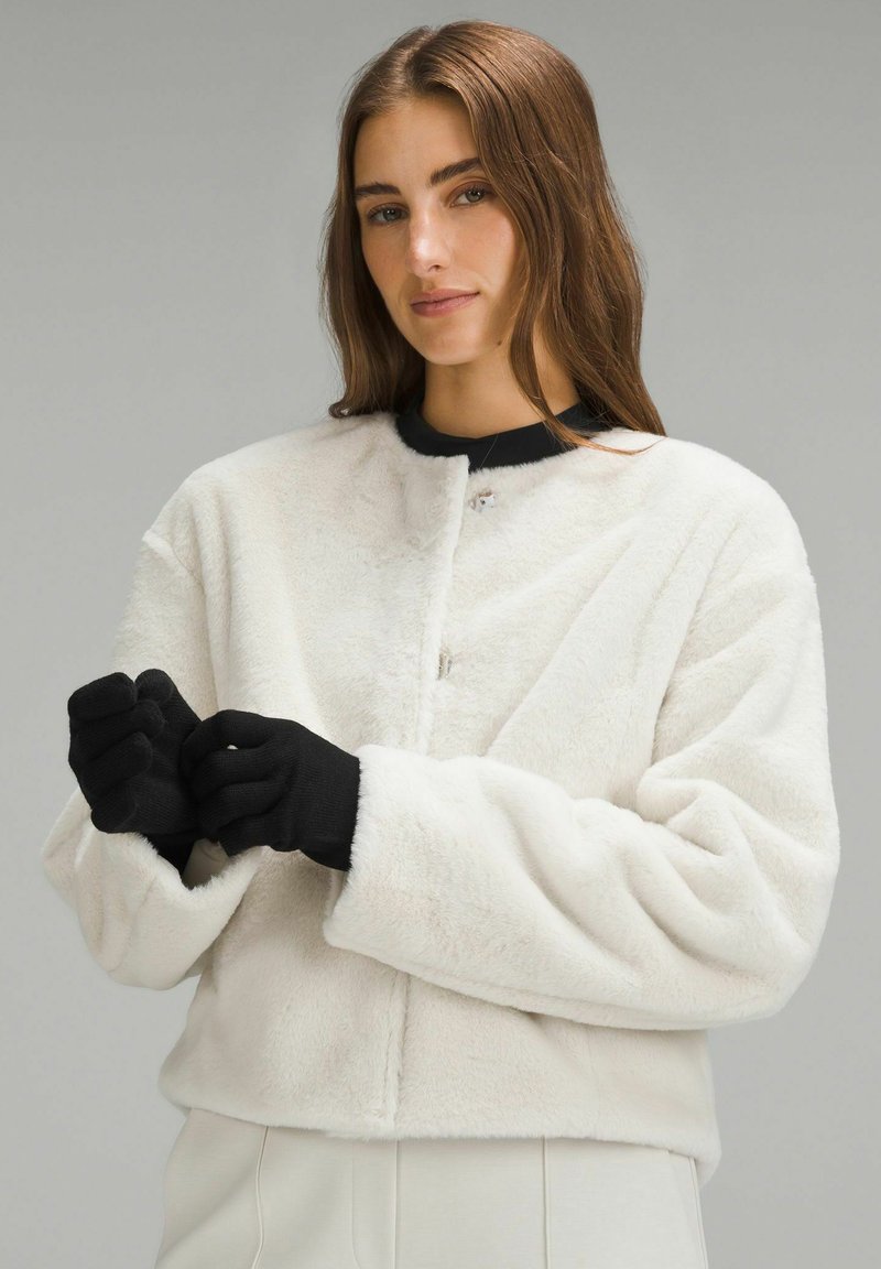 Biała futrzana kurtka z okrągłym dekoltem i zapięciem na haczyk. Posiada szerokie czarne mankiety i czarne rękawiczki. Miękka faktura, krótki fason.