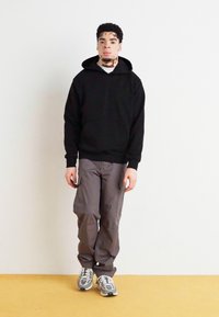 Sort hættebluse, grå cargo-bukser og grå sneakers. Casual pasform og blød tekstur med forkantet kangaroo-lomme og mange sidelommer.