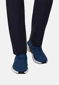 Blaue gestrickte Sneaker mit strukturiertem Muster, weißer Gummisohle und schwarzen Akzenten. Kombiniert mit dunkel gefärbter Hose.