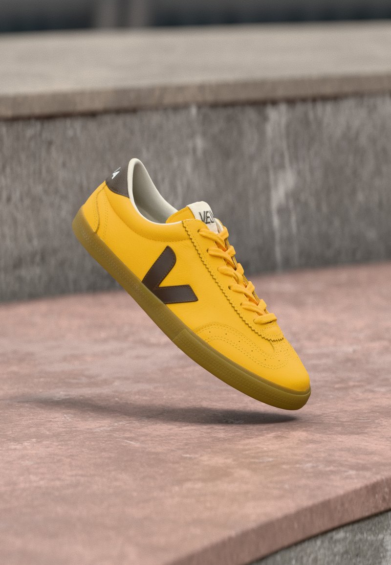 Baskets jaunes avec une tige en cuir lisse, des accents marron, un design à lacets, et une semelle en caoutchouc. Elles présentent un logo V contrastant sur le côté.