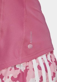 Gros plan sur une tenue de sport rose avec un haut en tissu texturé portant la mention « AEROREADY » et un short camouflage rose avec des rayures blanches verticales.