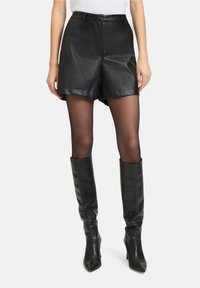 Zwarte leren high-waisted shorts met zijzakken, gecombineerd met sheer zwarte tights en lange, strakke zwarte leren kniehoogte laarzen.