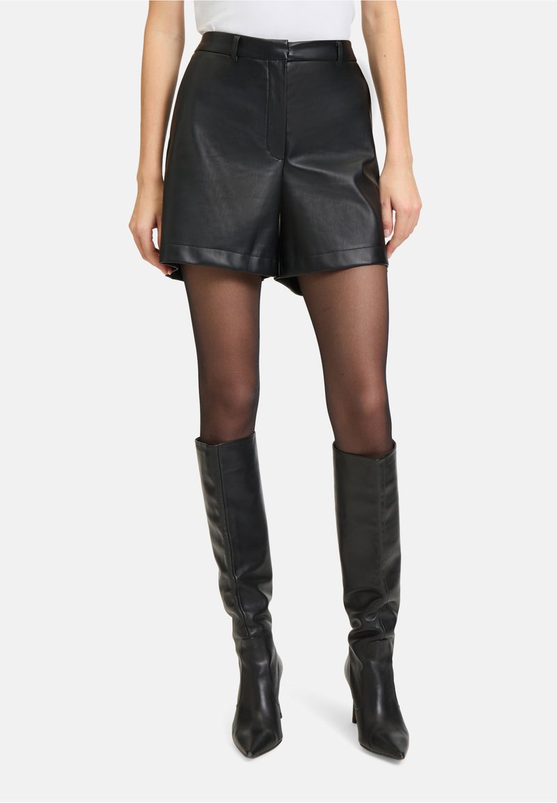 Zwarte leren high-waisted shorts met zijzakken, gecombineerd met sheer zwarte tights en lange, strakke zwarte leren kniehoogte laarzen.
