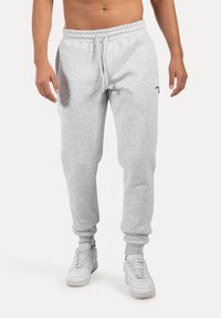 Grijze sweatpants met een elastische tailleband en verstelbaar trekkoord, met een taps toelopende pasvorm en manchet-ankels, gecombineerd met witte sneakers.