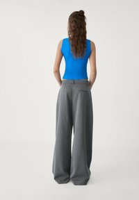 Top blu senza maniche abbinato a pantaloni grigi a vita alta e a gamba larga. Il tessuto sembra liscio con una leggera lucentezza e tasche sottili.