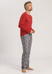 Röd långärmad tröja i kombination med mönstrade gråa pyjamasbyxor med blommönster. Mjuk tygkvalitet; inga synliga detaljer eller accenter.